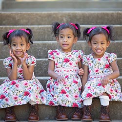 Alexandra, Alie, and Mila Reese sitting on steps with matching floral dresses, pink hair ribbons, and dark brown boots.
